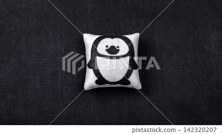 Handmade felt penguin ornament on white cushion against black background Handmade felt penguin ornament on white cushion against black background 142320207