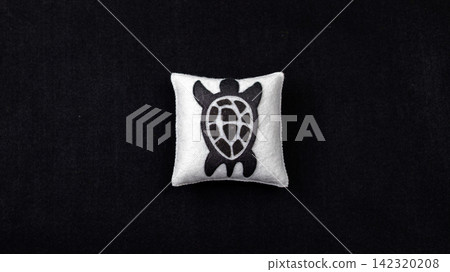 Handmade felt sea turtle ornament on white cushion against black background 142320208