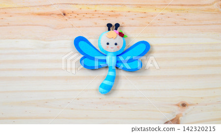 Cute handmade dragonfly toy on a wooden background with copy space Cute handmade dragonfly toy on a wooden background with copy space 142320215