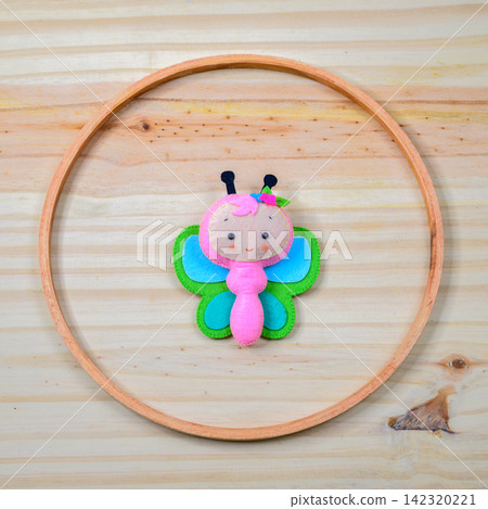 Handmade felt cute butterfly decoration arranged inside a circular wooden ring on a light wooden background Handmade felt cute butterfly decoration arranged inside a circular wooden ring on a light wooden background 142320221