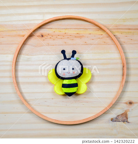 Handmade felt cute bee decoration arranged inside a circular wooden ring on a light wooden background 142320222
