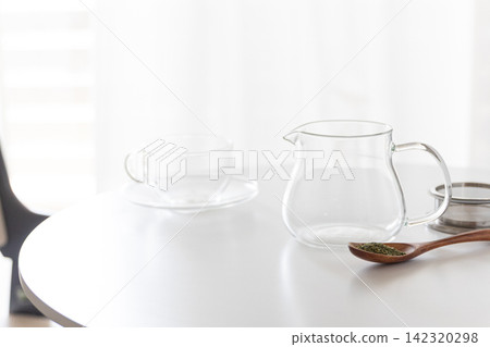 透明玻璃茶壺裡盛著綠茶葉,放在白色桌上。 透明玻璃茶壺裡盛著綠茶葉,放在白色桌上。 142320298