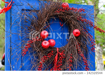 Handmade rustic wreath made of dry twigs red apples and berries hanging on vintage blue wooden door with copy space area. Handmade rustic wreath made of dry twigs red apples and berries hanging on vintage blue wooden door with copy space area. 142320544