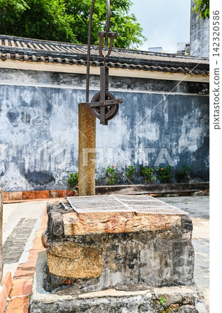 Ancient stone water well built in 1869 with rusted iron pulley mechanism inside traditional courtyard in Mandarin House 142320586