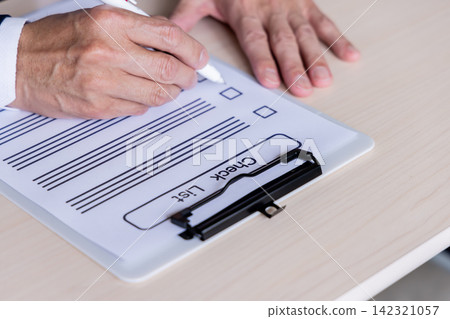 A business person's hands as they check items on a checklist with a pen. A business person's hands as they check items on a checklist with a pen. 142321057
