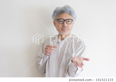 A senior man manages his health with water and medicine in hand. A senior man manages his health with water and medicine in hand. 142321133