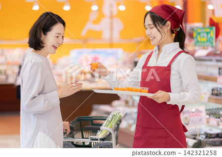 超市裡，一位面帶微笑的女店員向一位女顧客提供免費試飲。 142321258