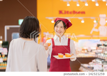 超市裡,一位面帶微笑的女店員向一位女顧客提供免費試飲。 超市裡,一位面帶微笑的女店員向一位女顧客提供免費試飲。 142321259
