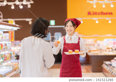 超市裡,一位面帶微笑的女店員向一位女顧客提供免費試飲。 超市裡,一位面帶微笑的女店員向一位女顧客提供免費試飲。 142321260