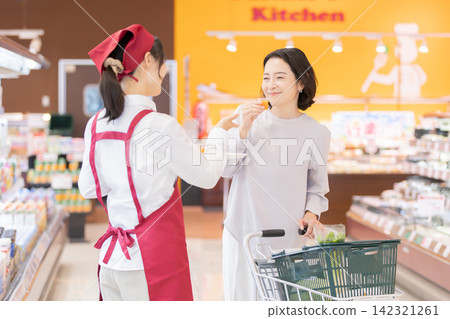 超市裡,一位面帶微笑的女店員向一位女顧客提供免費試飲。 超市裡,一位面帶微笑的女店員向一位女顧客提供免費試飲。 142321261