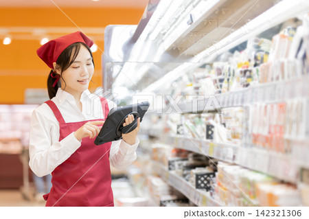 一名女店員使用平板電腦管理超市貨架上的庫存。 一名女店員使用平板電腦管理超市貨架上的庫存。 142321306