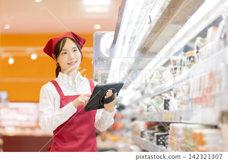 一名女店員使用平板電腦管理超市貨架上的庫存。 一名女店員使用平板電腦管理超市貨架上的庫存。 142321307