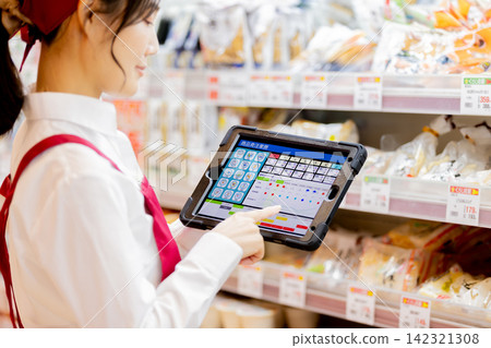 一名女店員使用平板電腦在超市貨架上訂購商品。 一名女店員使用平板電腦在超市貨架上訂購商品。 142321308