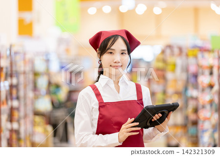 超市裡，一位女店員面帶微笑，手拿平板電腦工作。 142321309
