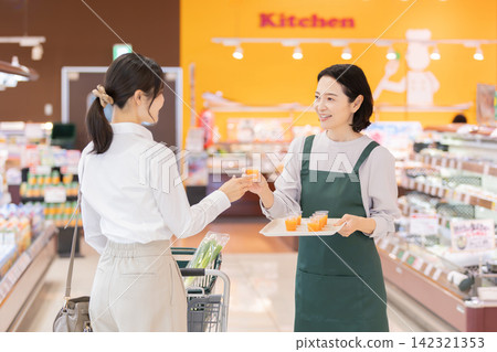 超市裡,一位面帶微笑的女店員向一位女顧客提供免費試飲。 超市裡,一位面帶微笑的女店員向一位女顧客提供免費試飲。 142321353