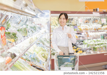 一位年輕女子正在超市蔬菜區推著購物車挑選商品。 一位年輕女子正在超市蔬菜區推著購物車挑選商品。 142321356