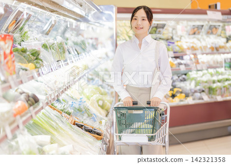 一位年輕女子正在超市蔬菜區推著購物車挑選商品。 一位年輕女子正在超市蔬菜區推著購物車挑選商品。 142321358