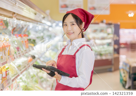 一名女店員正在超市蔬菜區操作平板電腦。 一名女店員正在超市蔬菜區操作平板電腦。 142321359