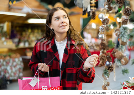Cheerful girl in plaid coat choosing handmade Christmas decorations at fair Cheerful girl in plaid coat choosing handmade Christmas decorations at fair 142321557