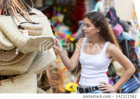 Female buyer looks at goods in outdoor shop, choose woven bag Female buyer looks at goods in outdoor shop, choose woven bag 142321562