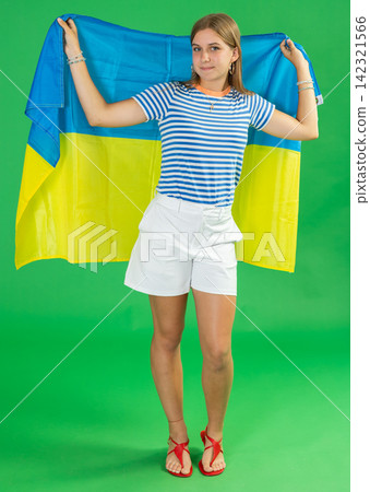 Teenage girl in white shorts with large flag of Ukraine posing on green background. Chroma key compositing Teenage girl in white shorts with large flag of Ukraine posing on green background. Chroma key compositing 142321566