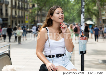 Happy young woman sitting on bench in Rambla Street of Barcelona Happy young woman sitting on bench in Rambla Street of Barcelona 142321584