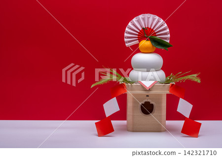 照片中,右側放置「鏡餅」(年糕供品),背景為紅白相間,旁邊還有一個三寶(支架)。 照片中,右側放置「鏡餅」(年糕供品),背景為紅白相間,旁邊還有一個三寶(支架)。 142321710