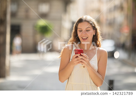 Happy young woman with mobile phone in her hands walking around city and taking pictures of sights 142321789