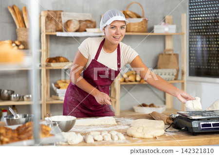 Girl baker cut small pieces of dough from large lump and put them on scales. Girl baker cut small pieces of dough from large lump and put them on scales. 142321810