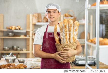 Young male baker holding baguettes in wicker basket Young male baker holding baguettes in wicker basket 142321821
