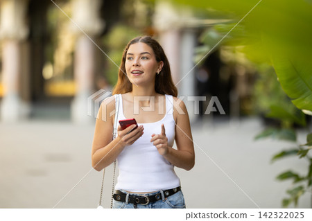 Young smiling girl with phone walks along city street Young smiling girl with phone walks along city street 142322025