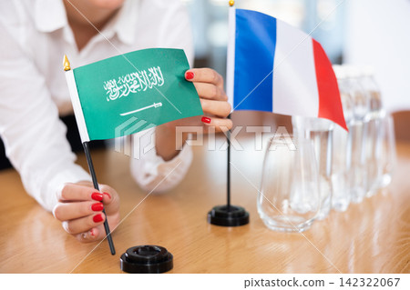 Woman secretary prepares an office for negotiations - she places flags of Saudi Arabia and France table Woman secretary prepares an office for negotiations - she places flags of Saudi Arabia and France table 142322067