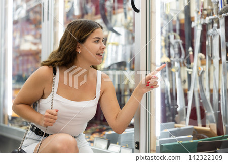 Interested young woman viewing various swords placed on display case Interested young woman viewing various swords placed on display case 142322109