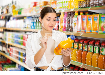 Young girl reading labels on bottles with juices in store 142322160