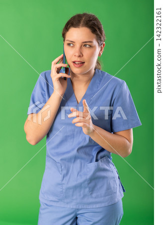 Nurse in blue uniform talking to someone on smartphone on green background Nurse in blue uniform talking to someone on smartphone on green background 142322161
