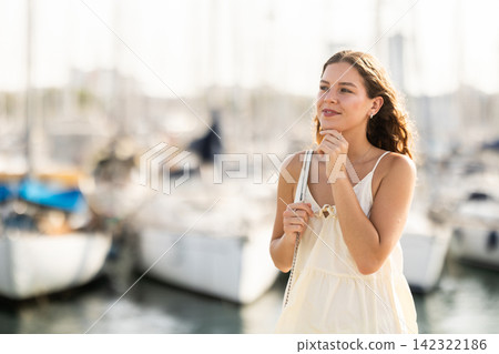 Happy young woman walking along the seaside promenade admiring city and yachts Happy young woman walking along the seaside promenade admiring city and yachts 142322186