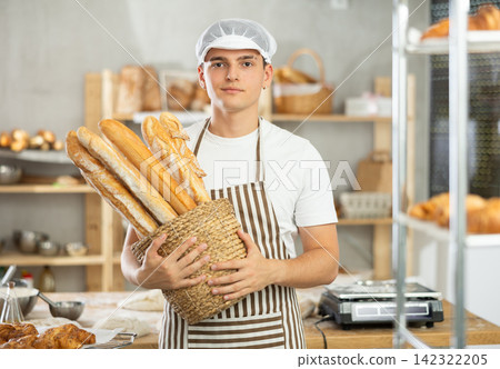 Happy male baker posing with basket of freshly baked baguettes in bakery, demonstrating concept of food industry and baker profession 142322205