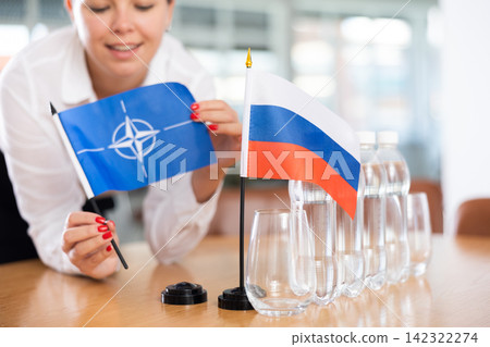 Unrecognizable girl sets midget flags of Russia and NATO before international negotiations Unrecognizable girl sets midget flags of Russia and NATO before international negotiations 142322274