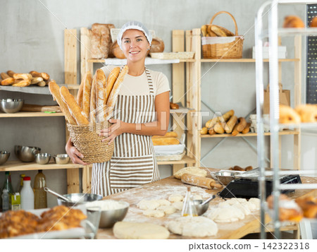 Dedicated young female baker holding freshly baked baguettes Dedicated young female baker holding freshly baked baguettes 142322318