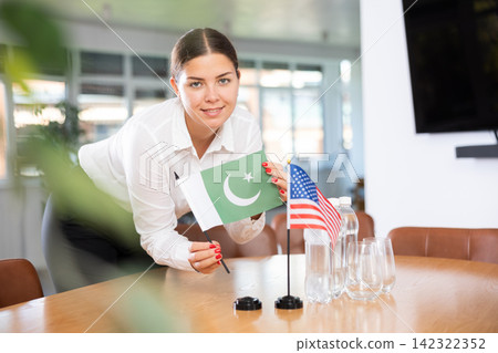 Young woman putting flags of Pakistan and USA on table in office Young woman putting flags of Pakistan and USA on table in office 142322352