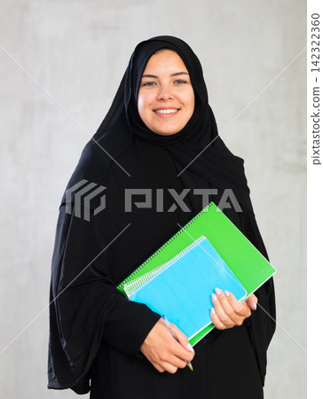 positive smiling girl in traditional black hijab stands and holds flock of colorful notebooks. positive smiling girl in traditional black hijab stands and holds flock of colorful notebooks. 142322360