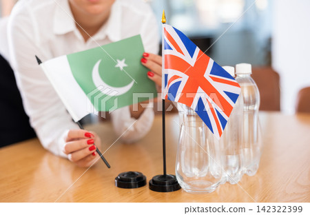 Little flag of Great Britain on table and flag of Pakistan put next to it by young woman Little flag of Great Britain on table and flag of Pakistan put next to it by young woman 142322399