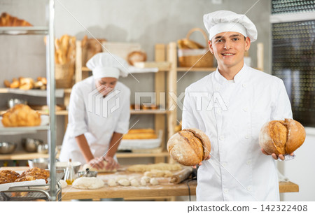 Young man are standing in kitchen with finished products two loaves of rye bread Young man are standing in kitchen with finished products two loaves of rye bread 142322408