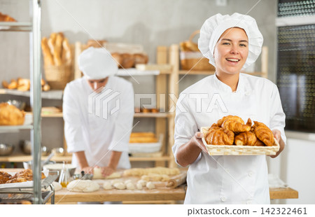Cheerful young female artisan baker presenting fluffy croissants in bakery 142322461