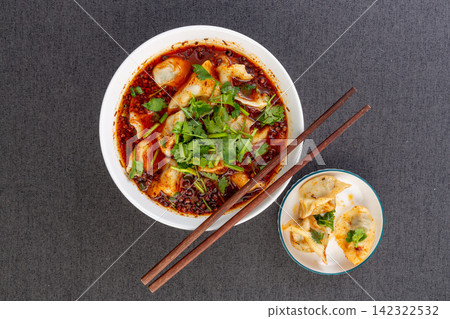 spicy dumpling soup with chili oil and coriander served in a bowl on black background spicy dumpling soup with chili oil and coriander served in a bowl on black background 142322532