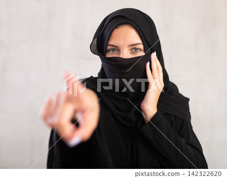 Young woman dressed in traditional islamic clothes with her face covered pointing to something Young woman dressed in traditional islamic clothes with her face covered pointing to something 142322620