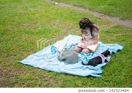 Young girl writing or drawing in notebook on a picnic blanket beside a dog in the park. Young girl writing or drawing in notebook on a picnic blanket beside a dog in the park. 142323464