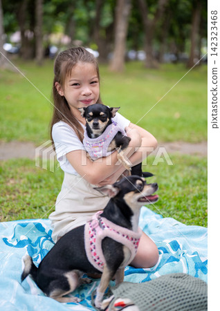 Young mixed race girl holds a small chihuahua dog while another dog stands beside her in the park. Young mixed race girl holds a small chihuahua dog while another dog stands beside her in the park. 142323468