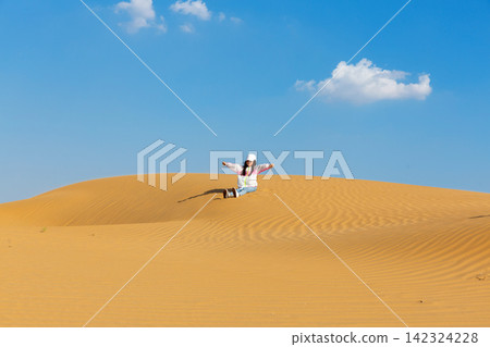 A little girl sliding down a massive sand dune in the desert under a clear blue sky. A little girl sliding down a massive sand dune in the desert under a clear blue sky. 142324228