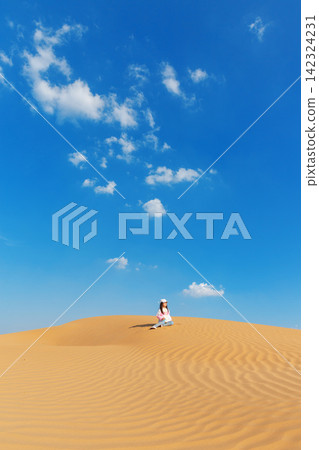 A little girl sliding down a massive sand dune in the desert under a clear blue sky. 142324231